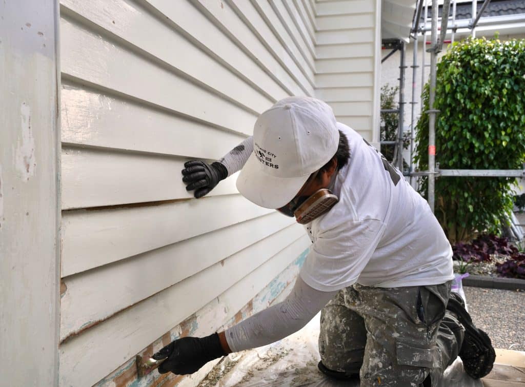 Painter stripping paint from weatherboards
