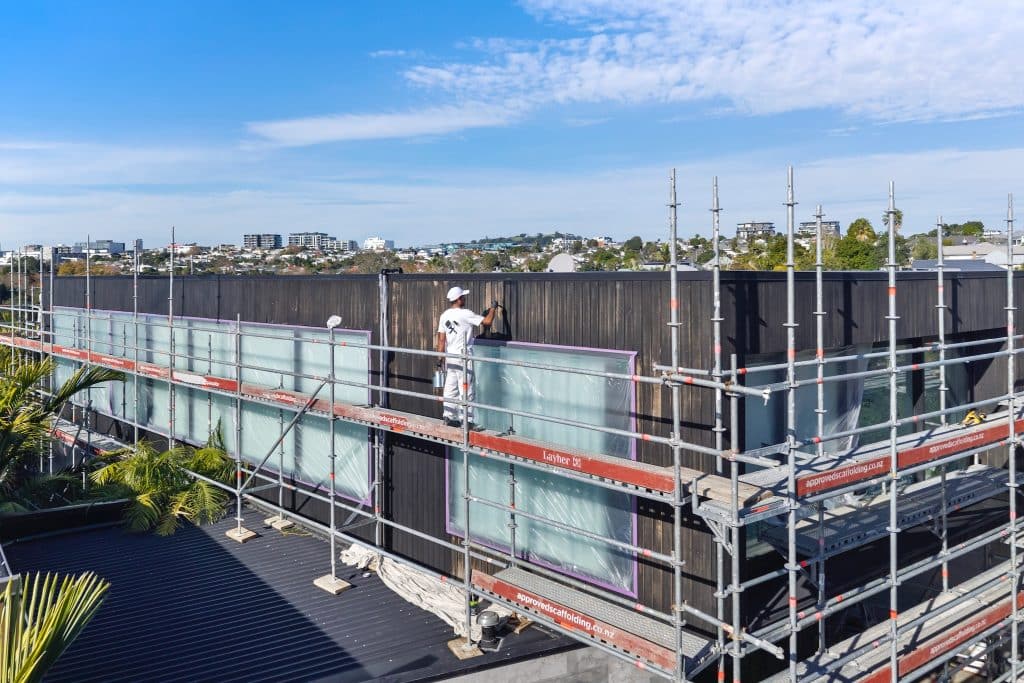 Painter on scaffold staining cedar home - Auckland City Painters