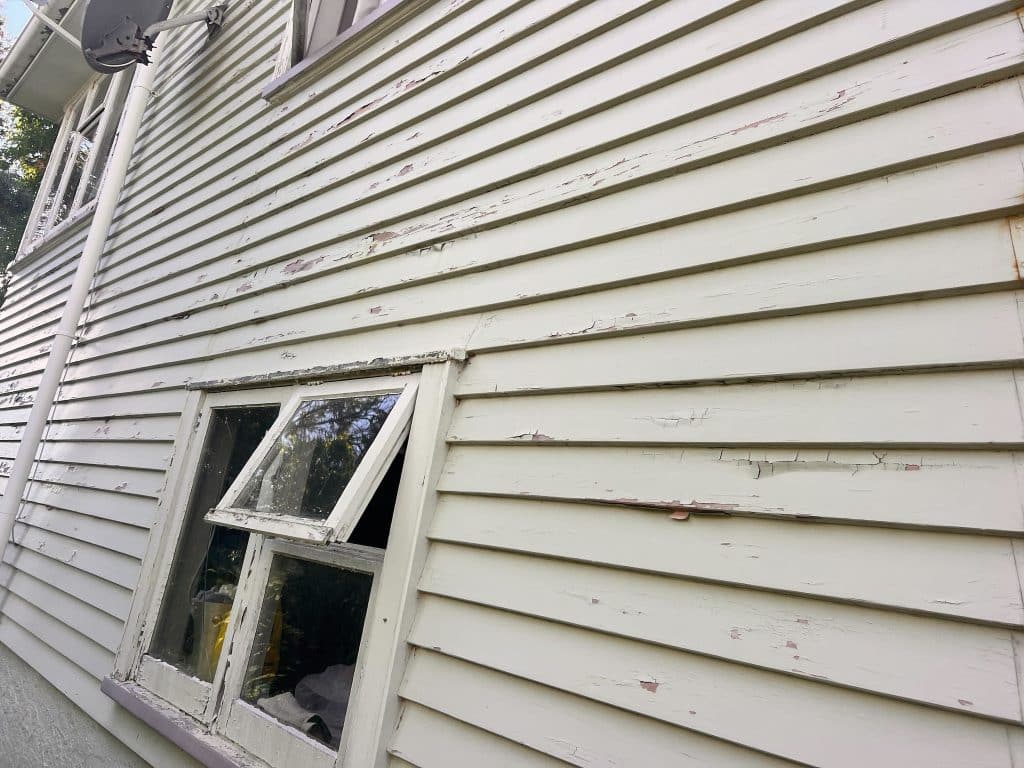 Side of a weatherboard home with wooden joinery where paint is peeling and delaminating