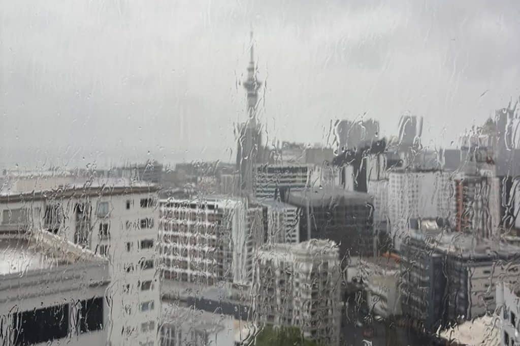 Rain streaking down a window overlooking Auckland's Sky Tower on a wet, overcast day